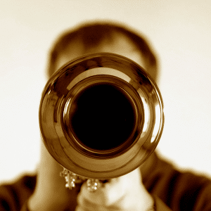 A man blowing his own trumpet. Front view looking down the bell of the trumpet which obscures the players face.
