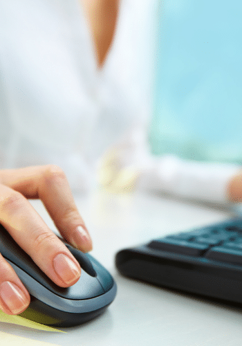 A lady at a desk on a computer clicking a mouse.