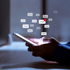 A man holding a mobile phone with holographic email enveleopes floating above the screen. One of the emails has a red notification with the number 12 in it.