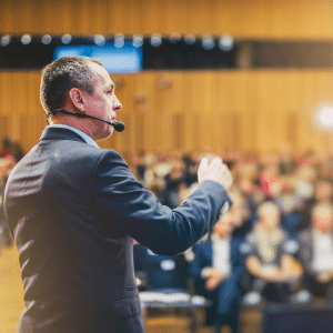 Man on stage with a mic talking to an audience.
