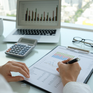 An image of a guys hands holding a pen who is auditing and cross referencing data.