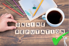 "Online Reputation" spelled out in wooden tiles on a desk with a pad and coloured pencils above and a large cup of coffee. A stick man is holding up a green tick in the bottom right corner.