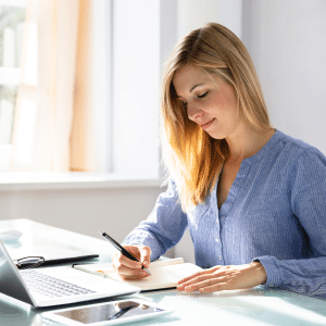 Happy and in flow. Young lady at her desk in a well lit room writing with a pen and pad.