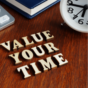 Value your time spelt out on a desk next to a clock.