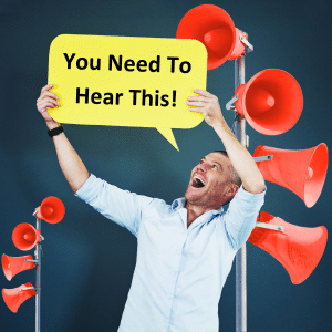 Happy man in a shirt holding up a sign saying "You need to hear this!". He's standing in front of several red lodspeakers.