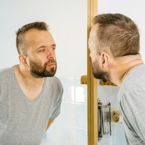 A close look at yourself in the mirror - man looking closley at himself. Negative feedback is an opportunity to improve what you see in the mirror.